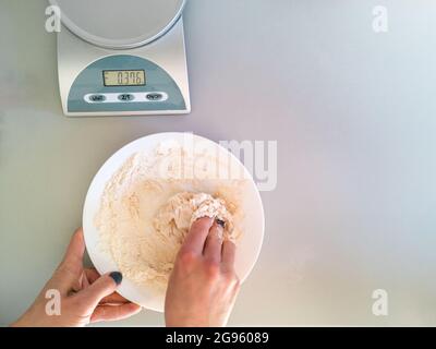 Una donna impasta l'impasto in una ciotola bianca con le mani Foto Stock