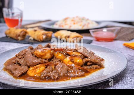 Piatto di cucina cinese, manzo in salsa con bambù e funghi cinesi, salsa dolce e aspre, riso 3 prelibatezze e involtini primaverili. Cibo asiatico Foto Stock