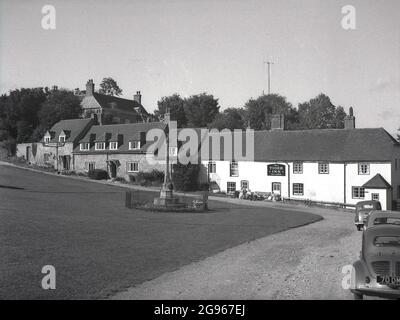 Anni '50, vista storica del villaggio verde, monumento in pietra e casa pubblica, la Tiger Inn a East Dean, a breve distanza dalle scogliere di Beachy Head sul South Downs, Eastbourne, East Sussex, Inghilterra, Regno Unito. Un villaggio di interesse storico, la Tiger Inn è un vecchio 15 ° secolo contrabbandieri inn, mentre ha detto che Sherlock Holmes si è ritirato lì. Foto Stock