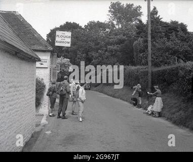 Anni '50, storico, un gruppo di rambler o escursionisti nei vestiti dell'epoca e alcuni con zaino in tela, in piedi in un vicolo fuori del Plow and Harrow Pub a Litlington, Polegate, sul South Downs, East Sussex, Inghilterra, Regno Unito. Foto Stock