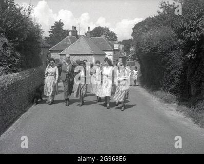 1950s, storico, un gruppo di ramblers, camminando su una corsia fuori del Plow and Harrow Pub a Litlington, Polegate, East Sussex, Inghilterra, Regno Unito, le donne che indossano le lunghe gonne dell'epoca. Un piccolo villaggio o villaggio sulle South Downs, è famoso per il suo grande gesso 'Cavallo Bianco', scolpito sul lato di Hindover Hill, noto come il Cavallo Bianco di Litlington. Foto Stock