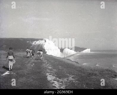 Anni '50, storici, membri di un club di rampicante, alcuni con ruckscaks tela, a piedi lungo la cima di Beachy Head', una famosa punta di gesso sul South Downs a Eastbourne, East Sussex, Inghilterra, Regno Unito. La più alta scogliera di mare di gesso in Gran Bretagna, i suoi dintorni ondulati bassi sono un bel posto per piacevoli passeggiate, con vista sulla Manica. Un'area di straordinaria bellezza naturale, nel 1929, con un atto del Parlamento, la terra è stata acquistata per salvaguardarne l'uso per le generazioni future Foto Stock