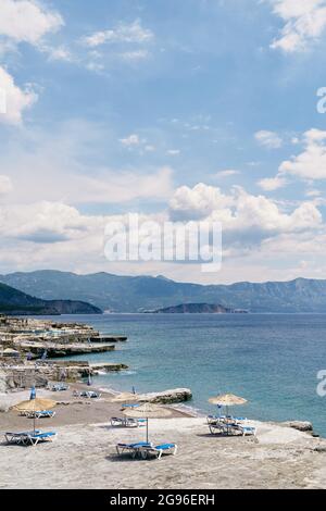 Vista sulla spiaggia rocciosa con lettini e ombrelloni con tetto in paglia vicino all'acqua Foto Stock