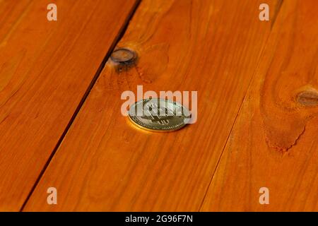 Medaglia d'oro di criptovaluta Bitcoin ai raggi del sole nascente sullo sfondo di un tavolo in legno arancione testurizzato. Concetto di nuovo digitale Foto Stock