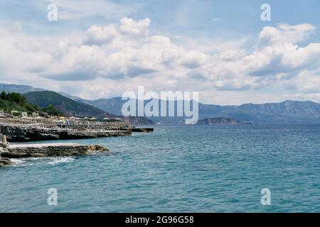 Vista dal mare alla costa rocciosa con lettini e ombrelloni con tetto in paglia Foto Stock