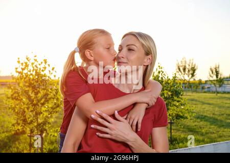 La ragazza adolescente si abbracca e bacia felicemente la madre in natura al tramonto Foto Stock