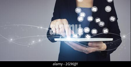 Concetto di marketing per e-mail e sms. Tavoletta bianca in mano di donna d'affari con segno di ologramma digitale su sfondo grigio. Azienda che invia molte e-mail o DIG Foto Stock