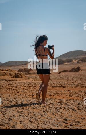 Uribia, la Guajira, Colombia - Maggio 28 2021: Giovane donna asiatica cammina guardando il suo telefono nel deserto Foto Stock