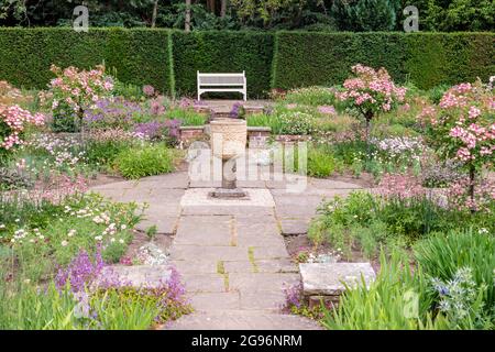 Angolo tranquillo di un giardino inglese segnalato formale con letti di fiori e un vaso di pietra. Foto Stock