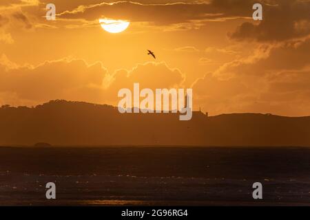 Tramonto sulla spiaggia di Loredo nel comune di Somo in provincia di Santander, con vista sul faro e le grandi nuvole Foto Stock