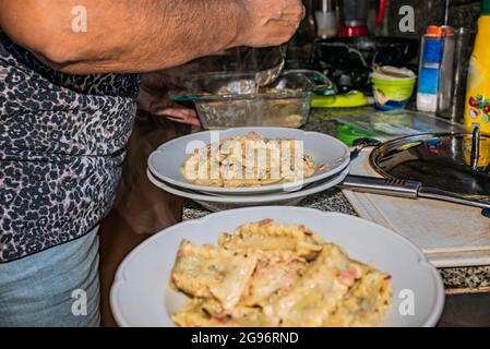 Donna che cucina pasta italiana fatta in casa, tagliatelle ripieni di spinaci e ricotta con salsa con panna, cipolle, aglio, prosciutto, spezie aromatiche e parmesa Foto Stock