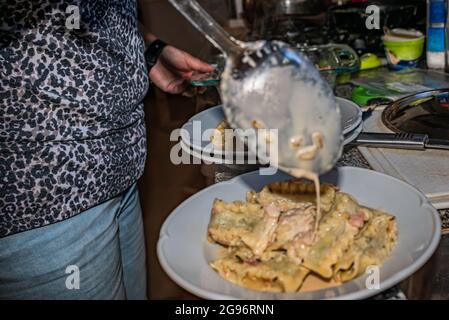 Donna che cucina pasta italiana fatta in casa, tagliatelle ripieni di spinaci e ricotta con salsa con panna, cipolle, aglio, prosciutto, spezie aromatiche e parmesa Foto Stock