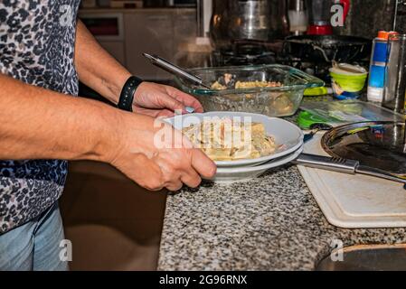 Donna che cucina pasta italiana fatta in casa, tagliatelle ripieni di spinaci e ricotta con salsa con panna, cipolle, aglio, prosciutto, spezie aromatiche e parmesa Foto Stock