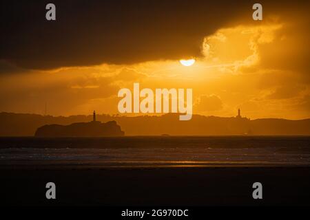 Tramonto sulla spiaggia di Loredo nel comune di Somo in provincia di Santander, con vista sul faro e le grandi nuvole Foto Stock