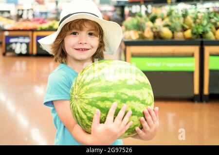 Capretto che tiene l'anguria nel supermercato contro il cibo stalla. Sorridente negozio di alimentari ragazzo positivo al supermercato Foto Stock