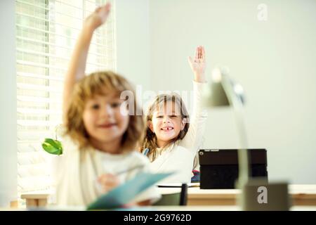 Carino piccoli alunni che alzano le mani durante la lezione. Bambini in classe a scuola Foto Stock