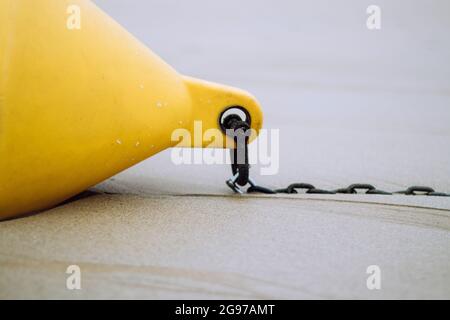 Una boa conica gialla con una catena sulla spiaggia sabbiosa bagnata Foto Stock