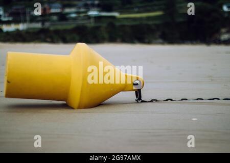 Una boa conica gialla con una catena sulla spiaggia sabbiosa bagnata Foto Stock