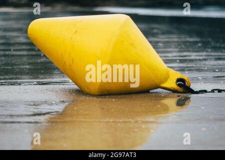 Una boa conica gialla con una catena sulla spiaggia sabbiosa bagnata Foto Stock