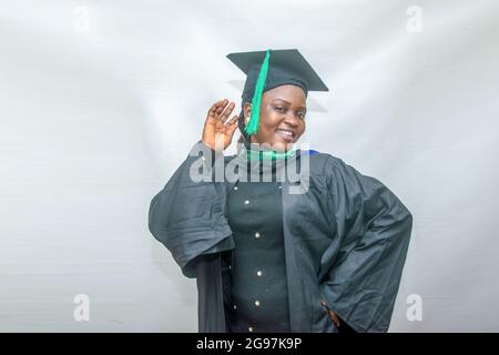 Foto di borsa di una donna africana laureata o laureata che sposta il suo corpo con gioia nel suo vestito nero di laurea Foto Stock