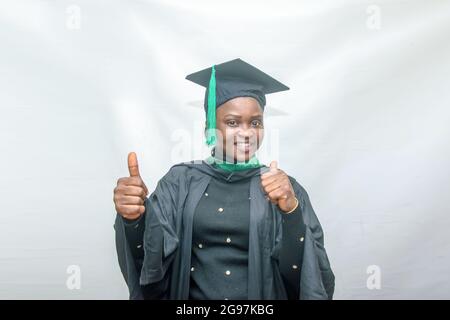 Foto di borsa di una donna africana laureata e/o laureata studenti nel suo vestito nero di laurea e gioiosamente facendo i pollici verso l'alto gesto Foto Stock