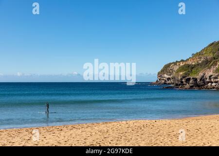 Uomo su un paddleboard al largo della costa della spiaggia di Warriewood a Sydney su un cielo blu inverno giorno, Sydney, Australia Foto Stock