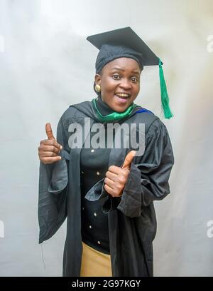 Foto di borsa di una donna africana laureata e/o laureata studenti nel suo vestito nero di laurea e gioiosamente facendo i pollici verso l'alto gesto Foto Stock