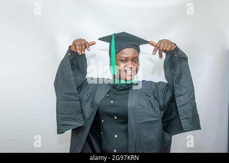 Foto di borsa di una donna africana laureata o laureata che sposta il suo corpo con gioia nel suo vestito nero di laurea Foto Stock