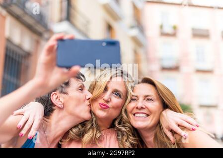 Donna adulta matura baciando la sua amica sulla guancia e prendendo un selfie Foto Stock