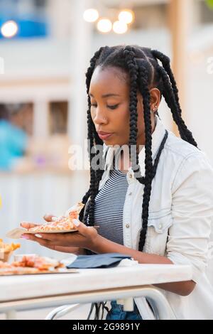 Donna afro-americana che raccoglie una fetta di pizza in una terrazza all'aperto Foto Stock