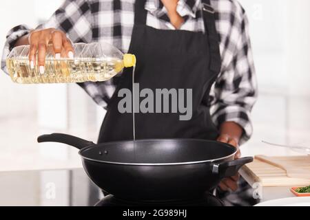 Primo piano della donna afro americana che versa l'olio da cucina in una padella profonda Foto Stock