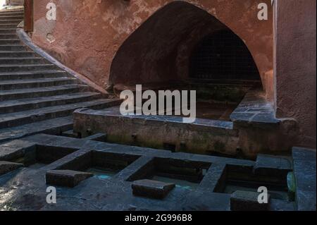 Una scalinata curva scende da Via Vittorio Emanuele al Lavatoio medievale di Cefalù, in Sicilia, dove l'acqua sorgiva del fiume Cefalino scorre attraverso lavabi con pendii in pietra per lo sfregamento di indumenti puliti da sporco ostinato e macchie. Il lavatoio ha antiche origini arabe ed è stato utilizzato per secoli dalle lavatrici di Cefalu. Secondo la leggenda locale, l'acqua proveniva dalle continue lacrime di una ninfa pianente piena di rimorsi per aver accidentalmente causato la morte del suo infedele amante. Foto Stock