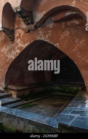 Archi moreschi che si ergono da mensole a gradini sopra la vasca a volta e gli antichi lavabi del Lavatoio medievale di Cefalù, Sicilia, Italia, ricordano un periodo pre-normanno in cui la città era sotto il controllo arabo. Per secoli, le lavatrici di Cefalu qui lavarono i vestiti in acque sorgive di montagna dal fiume Cefalino e lavarono i vestiti puliti da sporco ostinato e macchie sui pendii di pietra. Il poeta siciliano Vincenzo Auria descrisse l'acqua di Cefalino come "più pura dell'argento, più fredda della neve". Foto Stock
