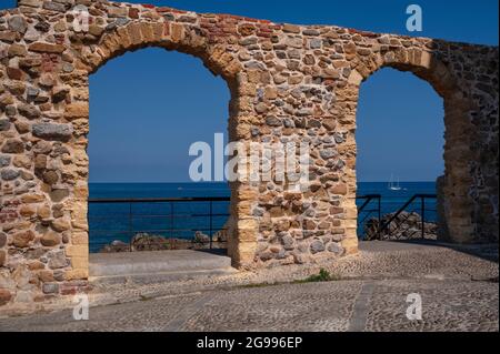 Gli archi di macerie restaurati in Piazza Marina, sopra il Porto Vecchio e Marina Beach, facevano parte delle mura difensive medievali che un tempo circondavano Cefalù, Sicilia, Italia. Essi ora si affacciano sul Mar Tirreno e offrono ‘maccesso al Sentiero sugli Scogli, che permette di ammirare in dettaglio fortificazioni molto più antiche, mura di 'Salita' costruite dal V secolo a.C. per scongiurare gli attacchi di mare. Enormi blocchi della lumachella locale o pietra di marmo di fuoco sono impilati fino a cinque - sei metri (16 - 20 piedi) di altezza. Foto Stock