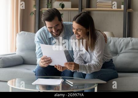 Una coppia sorridente si siede sul divano leggendo ha ricevuto una lettera formale Foto Stock