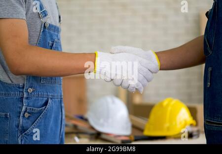 Carpentieri con guanto di protezione che scuotono le mani dopo aver terminato il lavoro. Un casco di costruzione bianco e giallo è stato posto sul tavolo sullo sfondo. Foto Stock