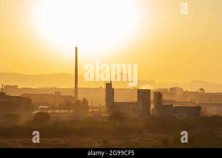 Paesaggio con sfondo industriale, fabbriche, camini, magazzini; illuminato da un grande sole, creando un'atmosfera di alta temperatura ambiente. Foto Stock