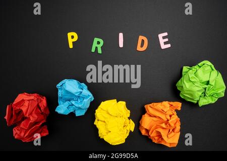 Alcuni fogli di carta colorata sgualcita e la parola Pride su una superficie nera Foto Stock