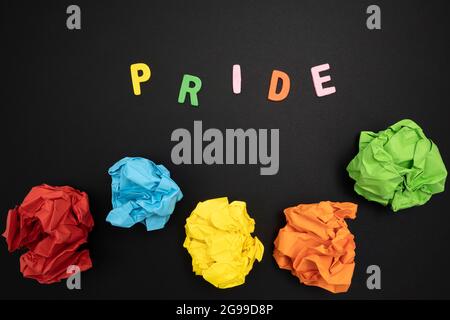 Alcuni fogli di carta colorata sgualcita e la parola Pride su una superficie nera Foto Stock