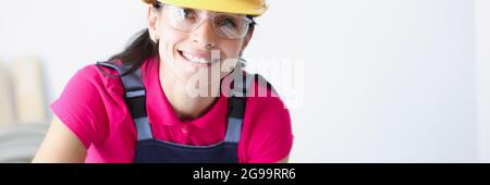 Sorridente lavoratrice di costruzione femminile in casco giallo curvato su progetti Foto Stock