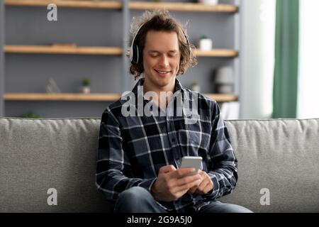 Millennial Man godersi la musica utilizzando il telefono indossando le cuffie a casa Foto Stock