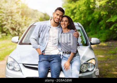 Uomo arabo amorevole e donna seduta sul cofano auto, abbracciando Foto Stock