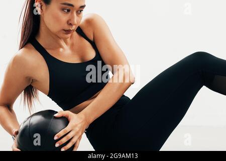 Primo piano di giovane donna asiatica che si esercita con la palla di medicina al chiuso Foto Stock