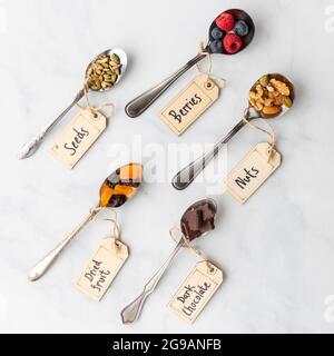 Vista dall'alto verso il basso dei cucchiai posti diagonalmente, ripieni di vari ingredienti sani comunemente usati nelle ciotole lisce. Foto Stock