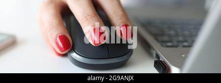 Donna con manicure rosso che tiene il mouse del computer vicino al closeup del laptop Foto Stock