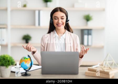 La videochiamata di Manager Lady parla con il computer portatile indossando le cuffie in interni Foto Stock