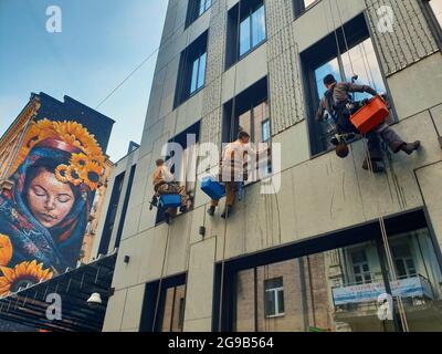 Kiev, Ucraina-28 aprile 2018: Tre pulitore di finestra sospeso in alto in un cablaggio di sedile su una corda di discesa lavando le finestre dell'edificio. Ragazza WIT Foto Stock