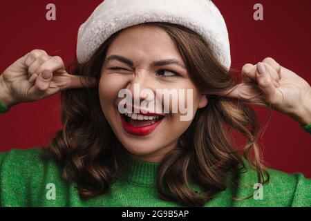 Attraente giovane donna allegra che indossa il cappello di santa isolato su sfondo rosso, grimacing Foto Stock