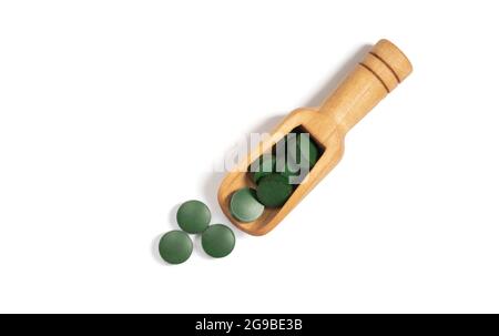Confetti verdi di Spirulina in un cucchiaio di legno isolato su sfondo bianco. Compresse di clorella. Vista dall'alto, disposizione piatta. Foto Stock