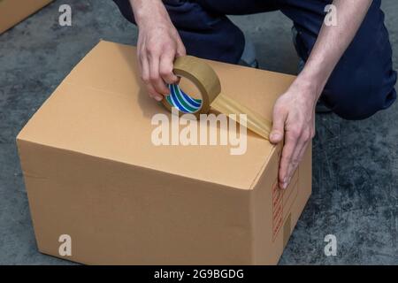 Scatole di imballaggio con nastro. Incollaggio del nastro per condotti su una scatola di cartone Kraft. Primo piano della scatola di cartone sigillante con nastro per condotti. Foto Stock